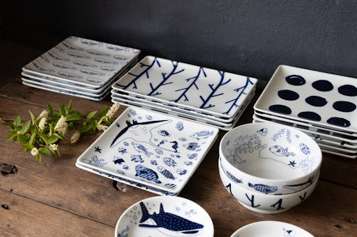 Blue-and-white Hasami porcelain plates and bowls with traditional Japanese patterns displayed on a wooden table.